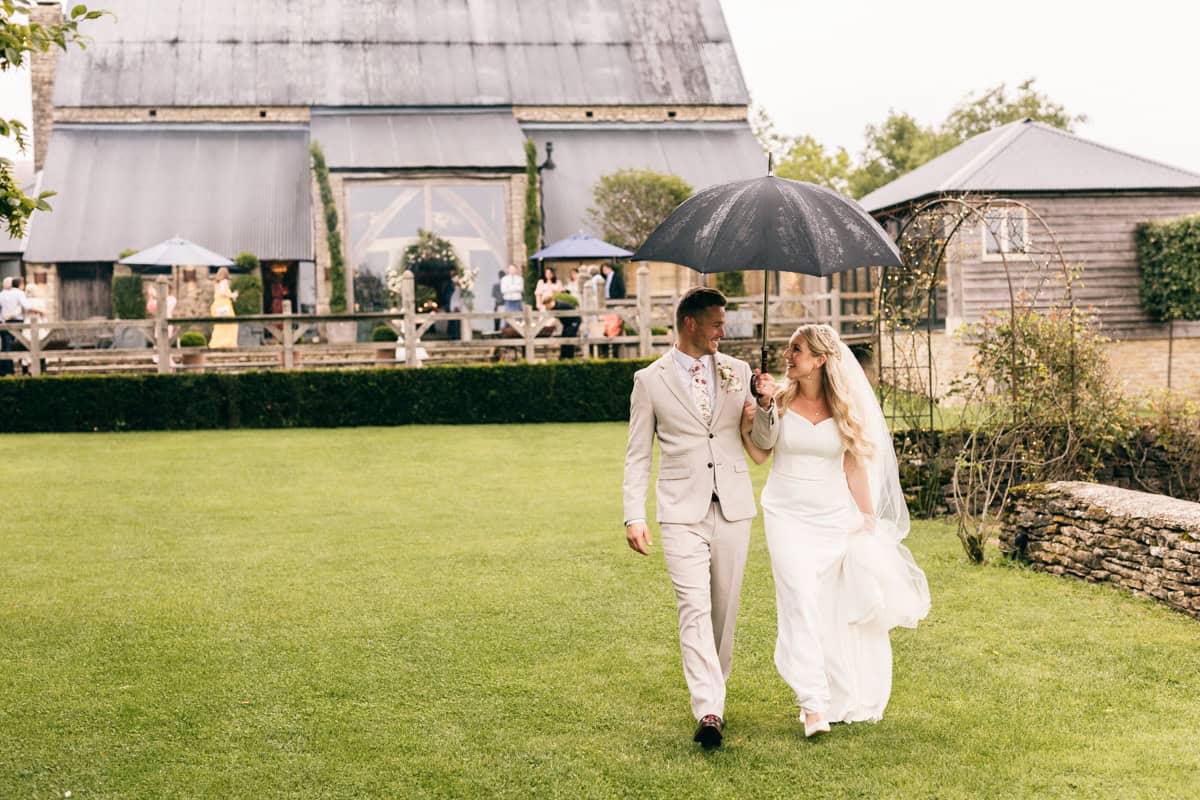 Wedding couple walking in the rain with umbrella at Cripps Barn.